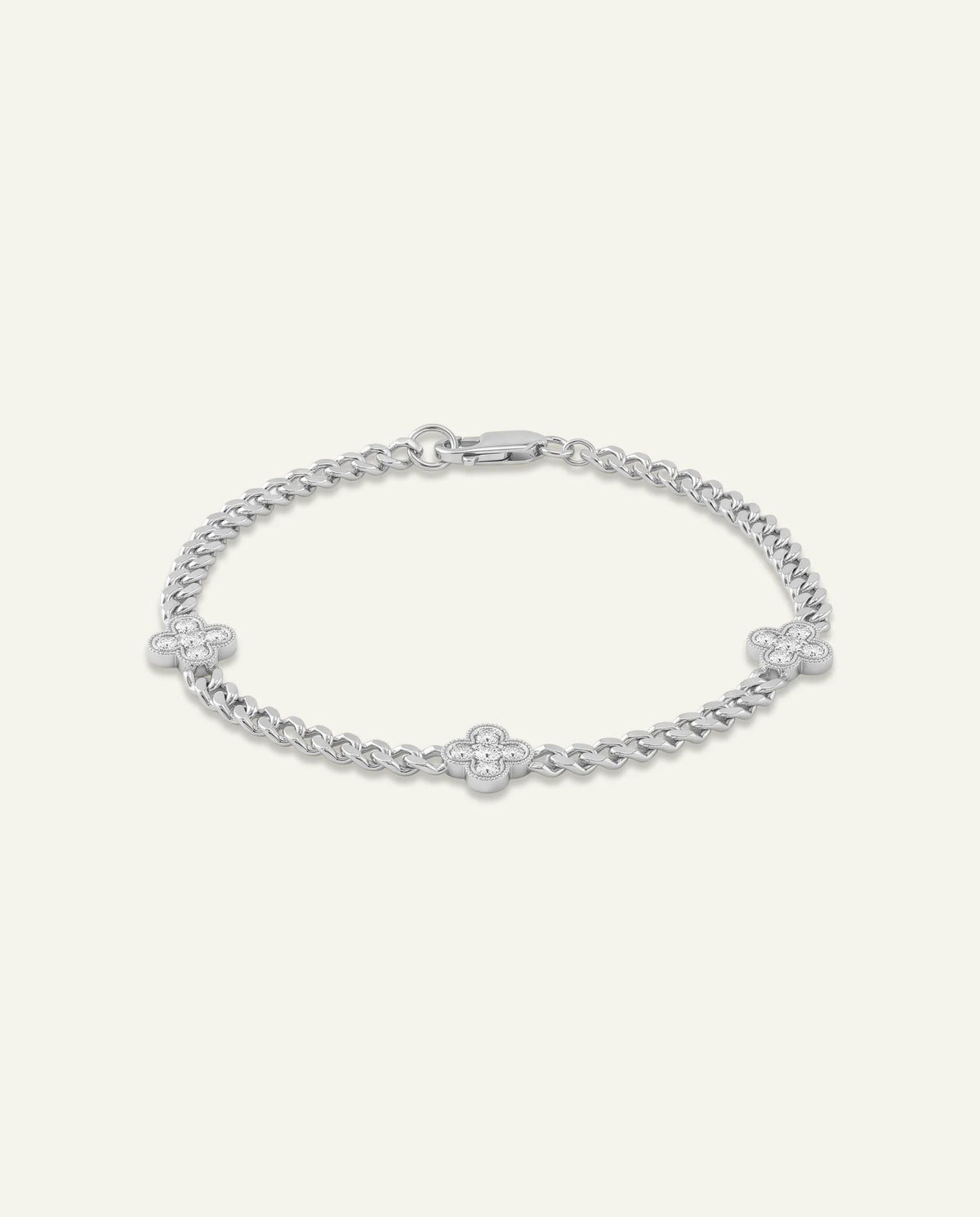 A silver-toned chain bracelet featuring three small clover motifs, one of which is set with a clear gemstone, displayed on a light cream background.