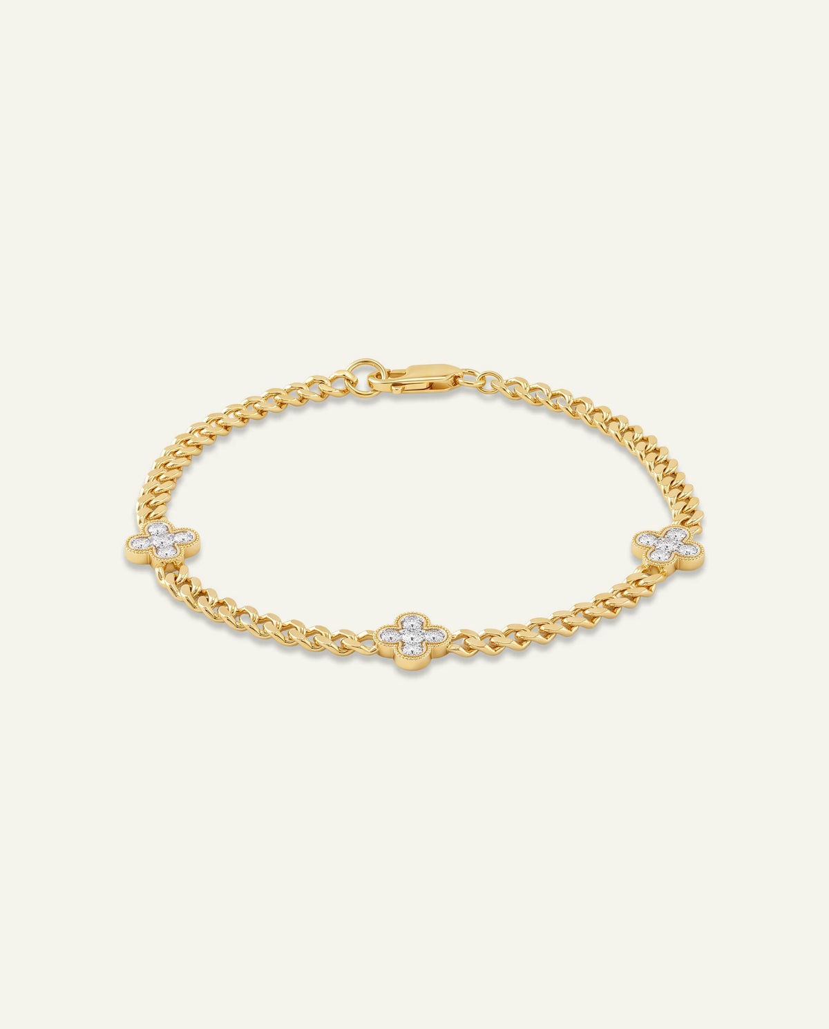 A gold chain bracelet with three small clover motifs, each set with a clear stone, displayed on a light cream background.
