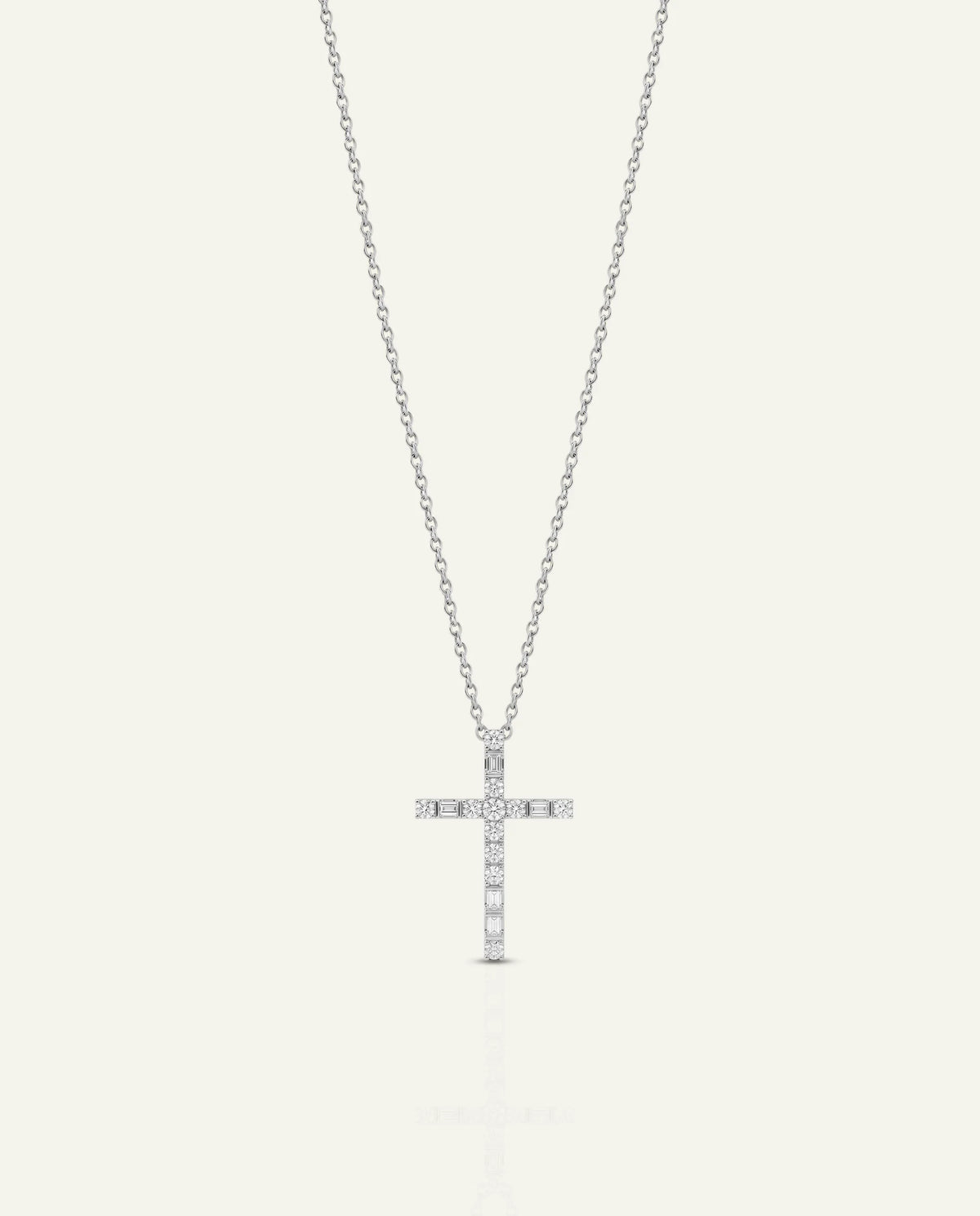 A delicate silver cross pendant necklace adorned with small clear stones, suspended from a fine silver chain against a light off-white background.