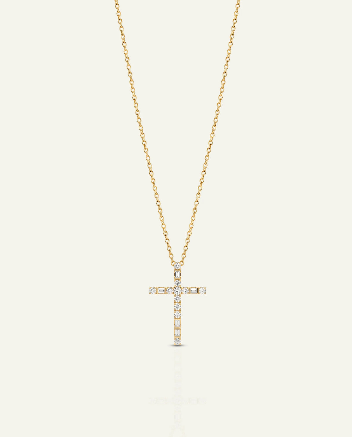 A delicate gold cross pendant necklace adorned with small clear stones, suspended from a fine gold chain against a light cream background.