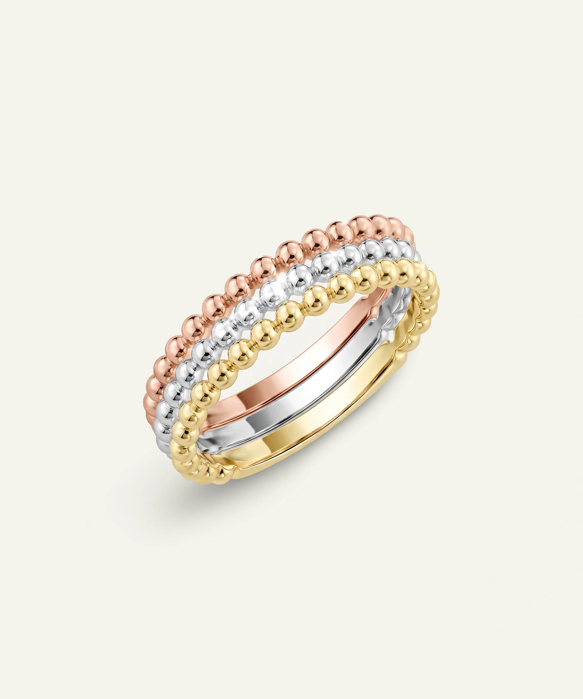 A set of three stacked beaded rings in yellow gold, rose gold, and white gold, featuring a row of clear round-cut gemstones on the outer bands, photographed on a light cream background.
