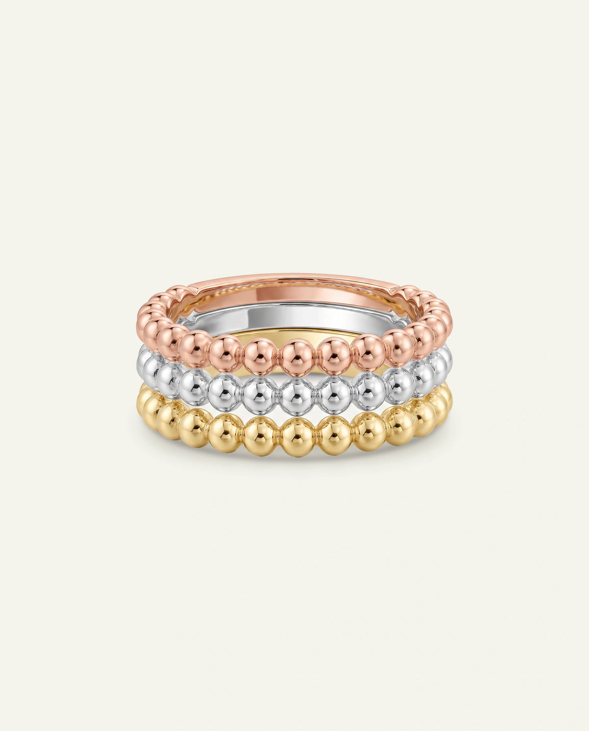 Three stacked beaded rings in rose gold, silver, and yellow gold, displayed on a light cream background.