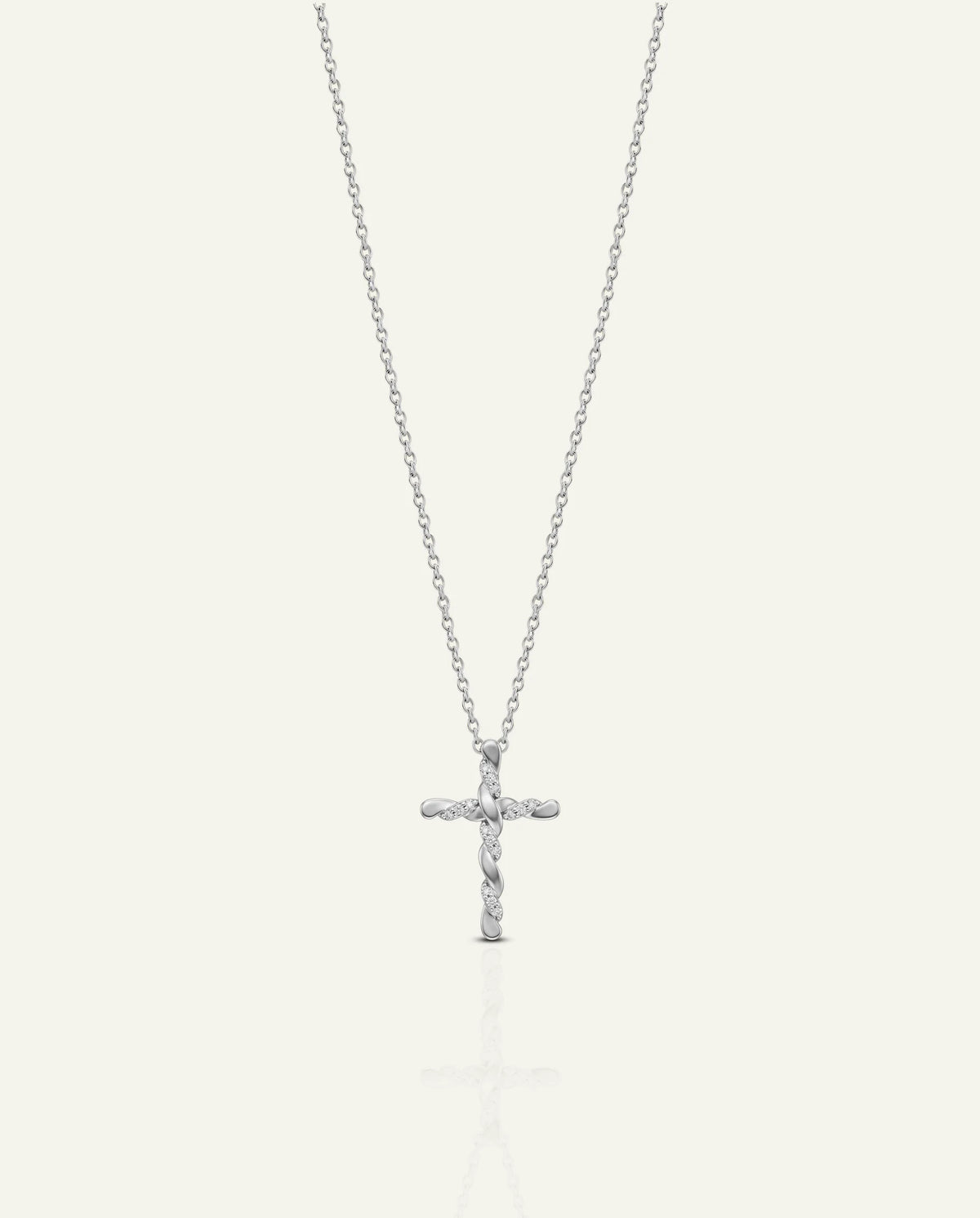 A silver cross pendant necklace with small clear stones, suspended from a delicate silver chain against a light off-white background.