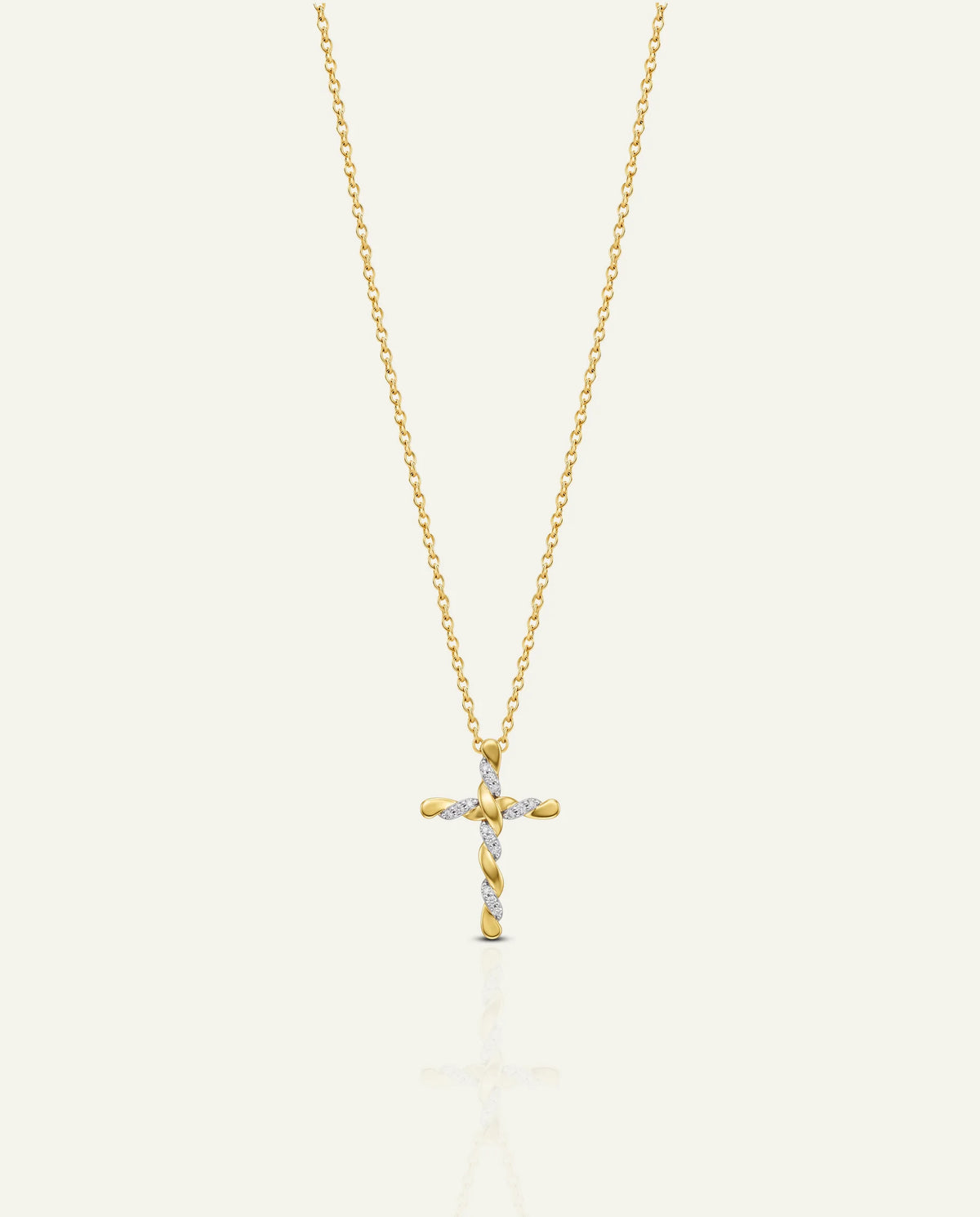 A delicate gold cross pendant necklace with small clear stones, suspended from a fine gold chain against a light cream background.