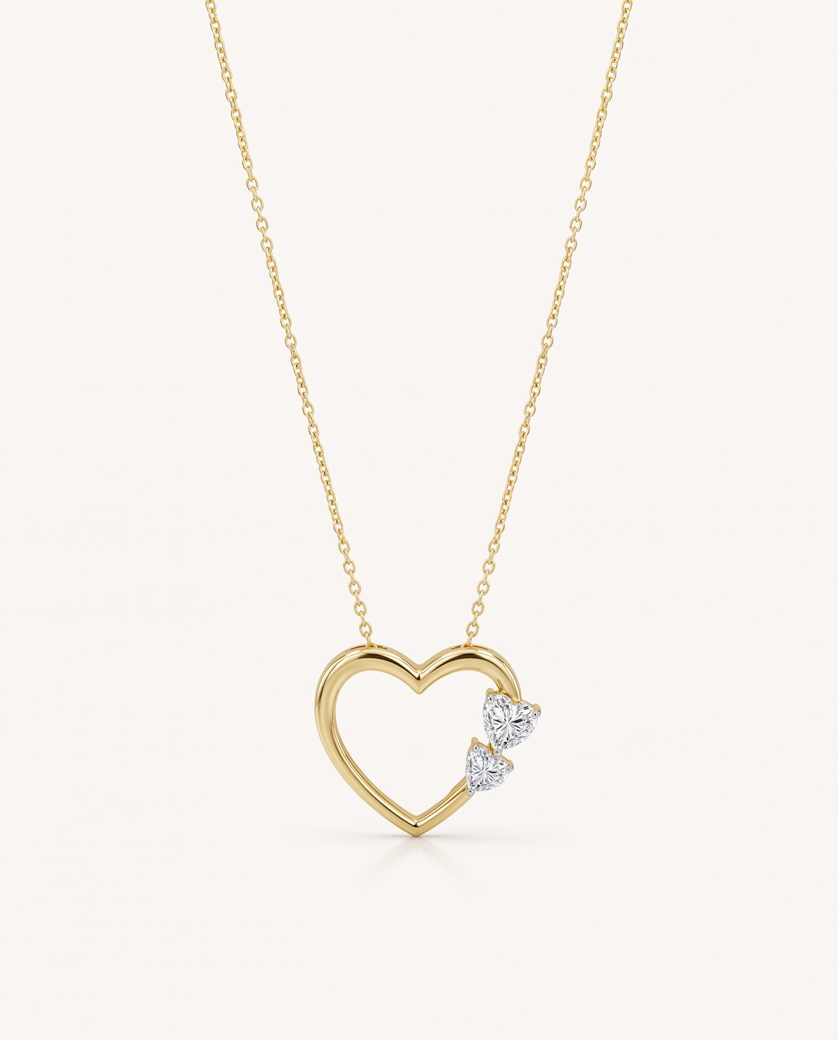 A delicate gold necklace featuring an open heart pendant adorned with two small clear heart-shaped gemstones on the right side, set against a solid off-white background.