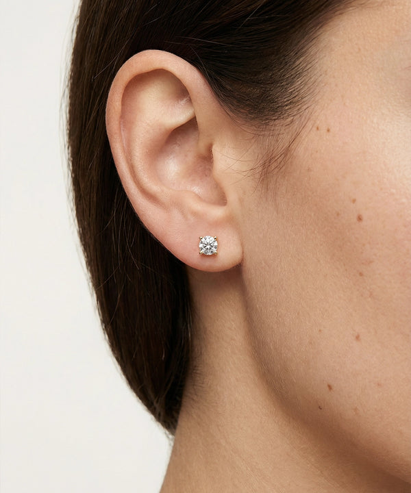 Close-up of an ear wearing a diamond stud earring on a plain background
