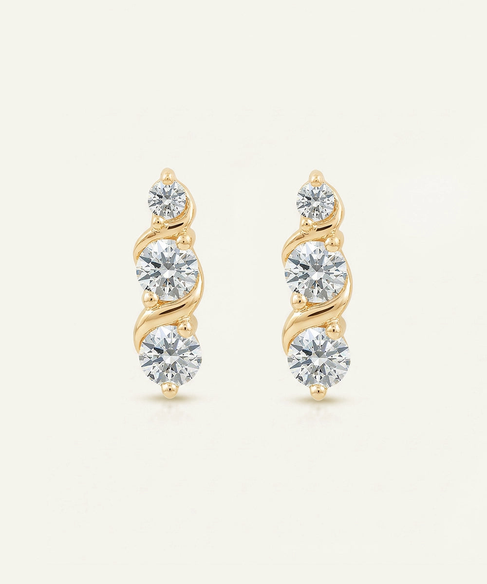 Pair of gold earrings with clear gemstones on a light beige background