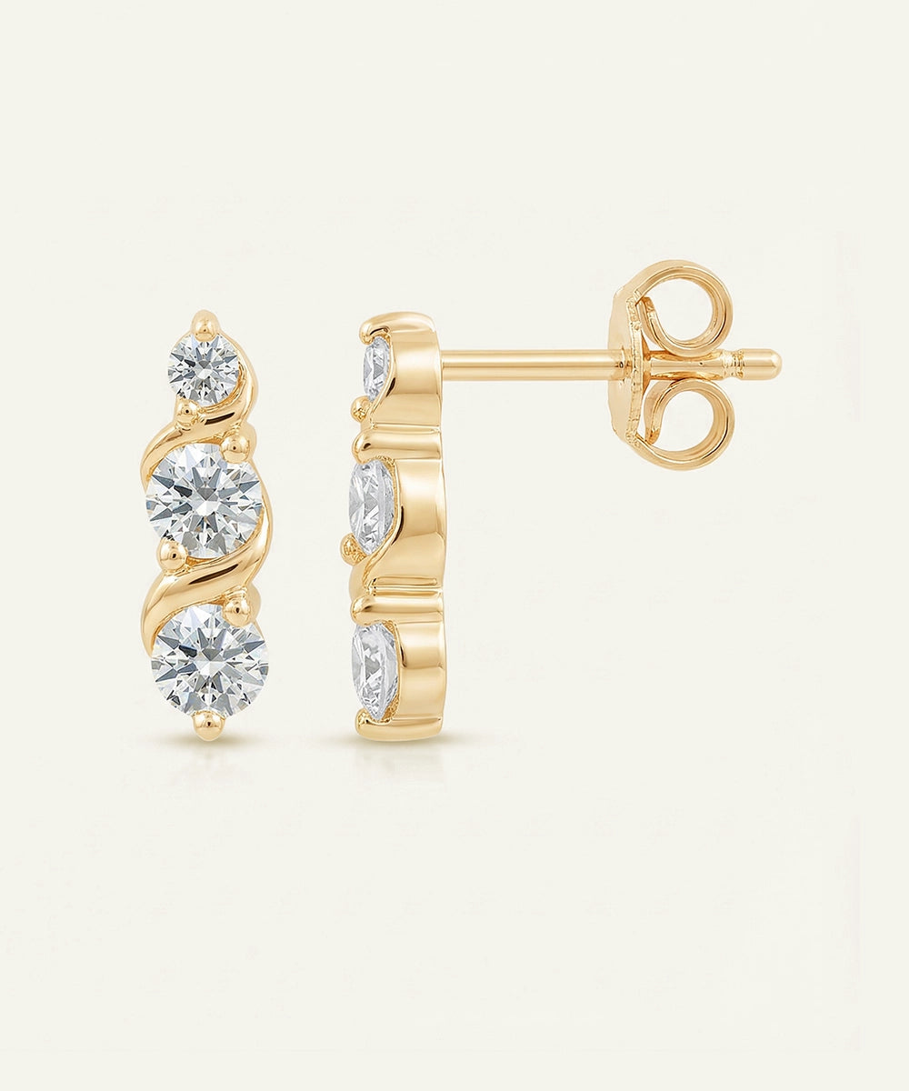 Gold earrings with clear gemstones on a light beige background