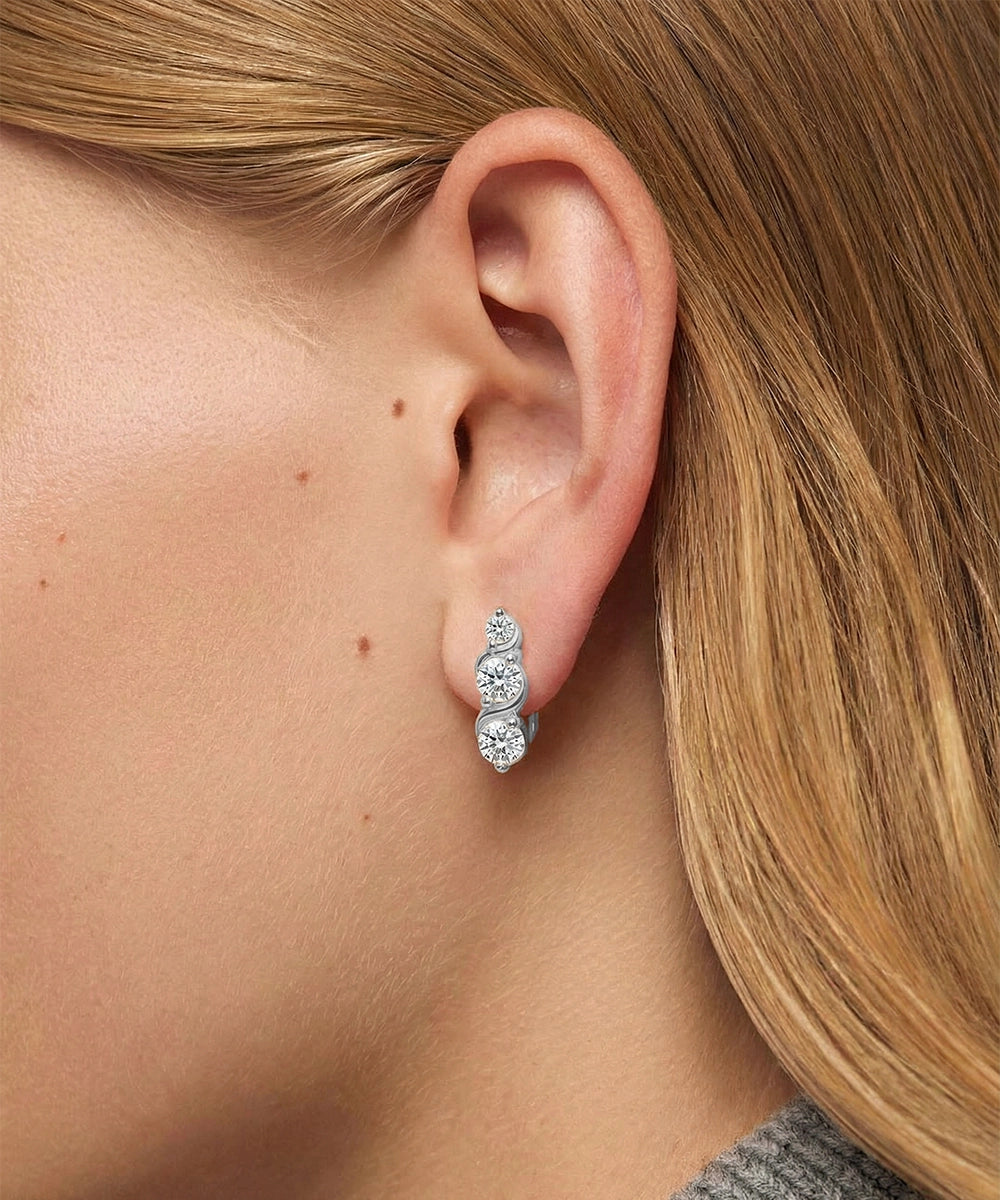 Close-up of an ear wearing a silver earring with three diamonds, blonde hair partially visible.
