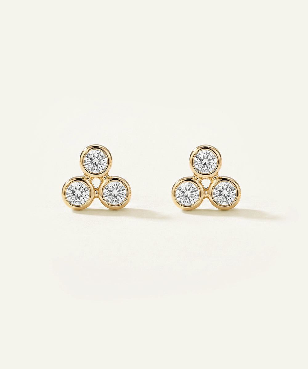 Pair of gold earrings with three round diamonds on a light beige background