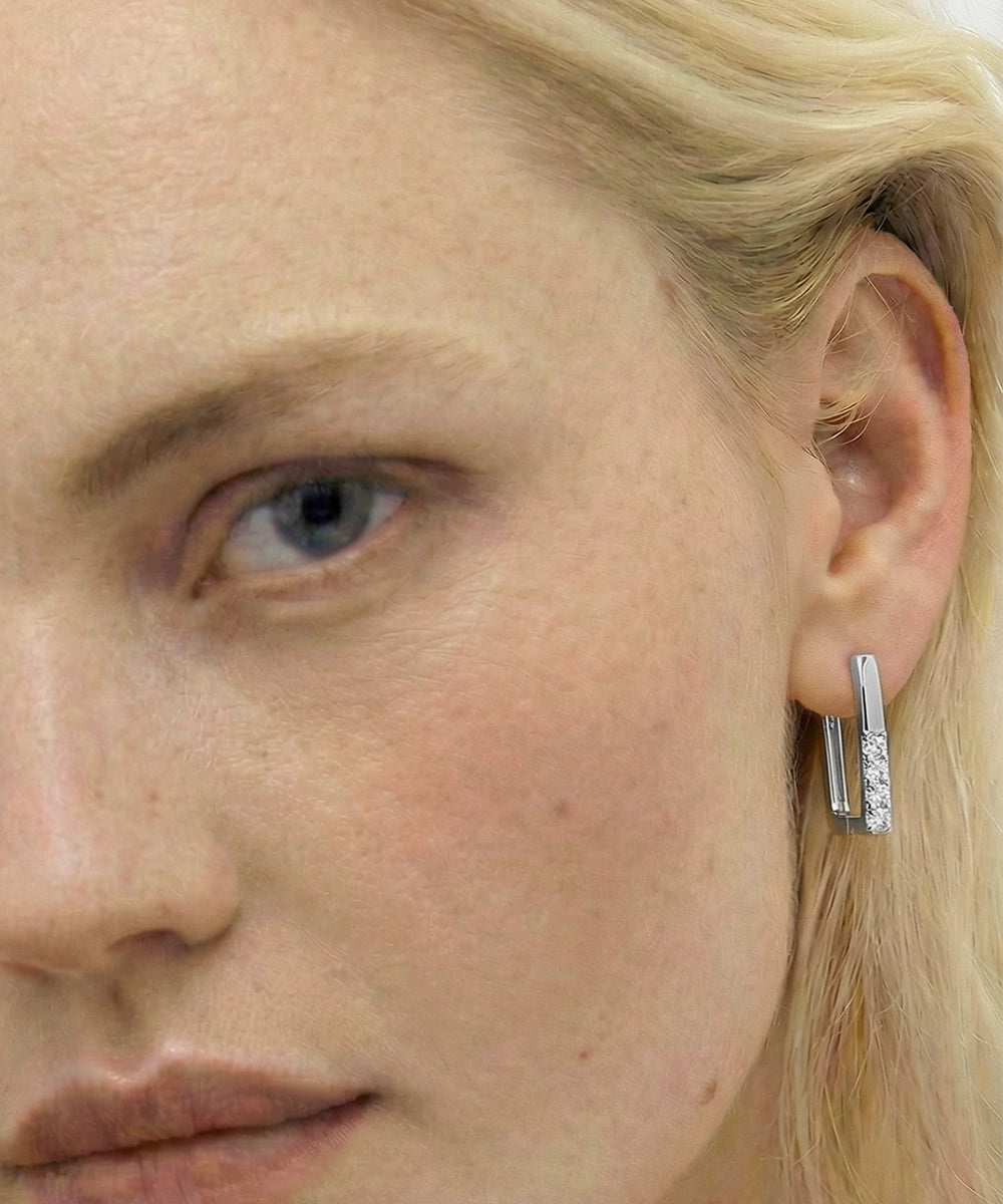 Close-up of a person wearing a silver hoop earring with a small gemstone.
