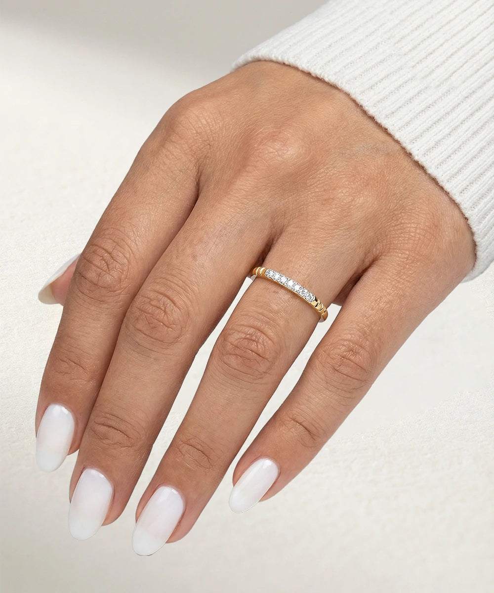 Hand wearing a gold ring with diamonds on a neutral background