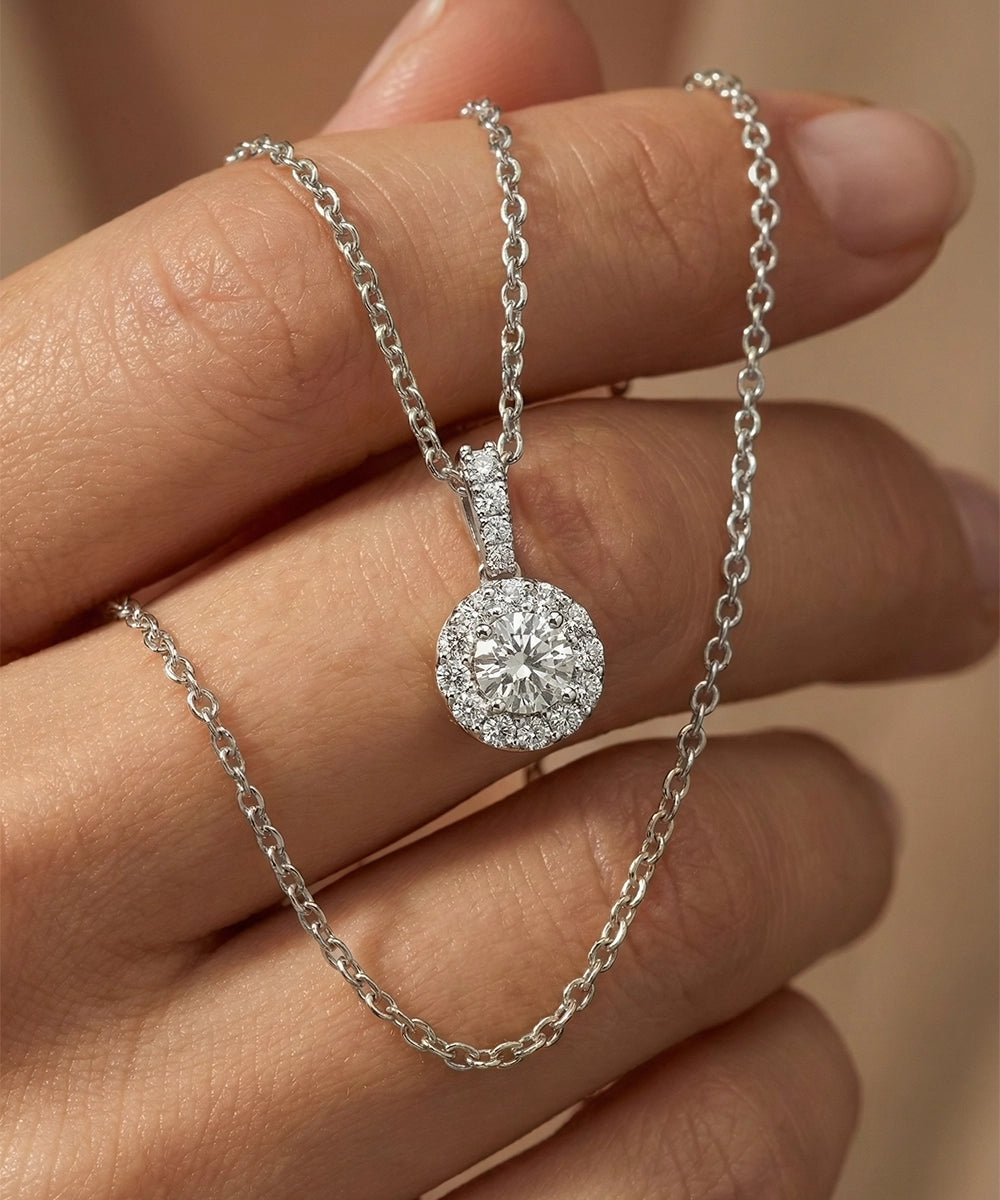 Silver necklace with a diamond pendant held between fingers against a neutral background