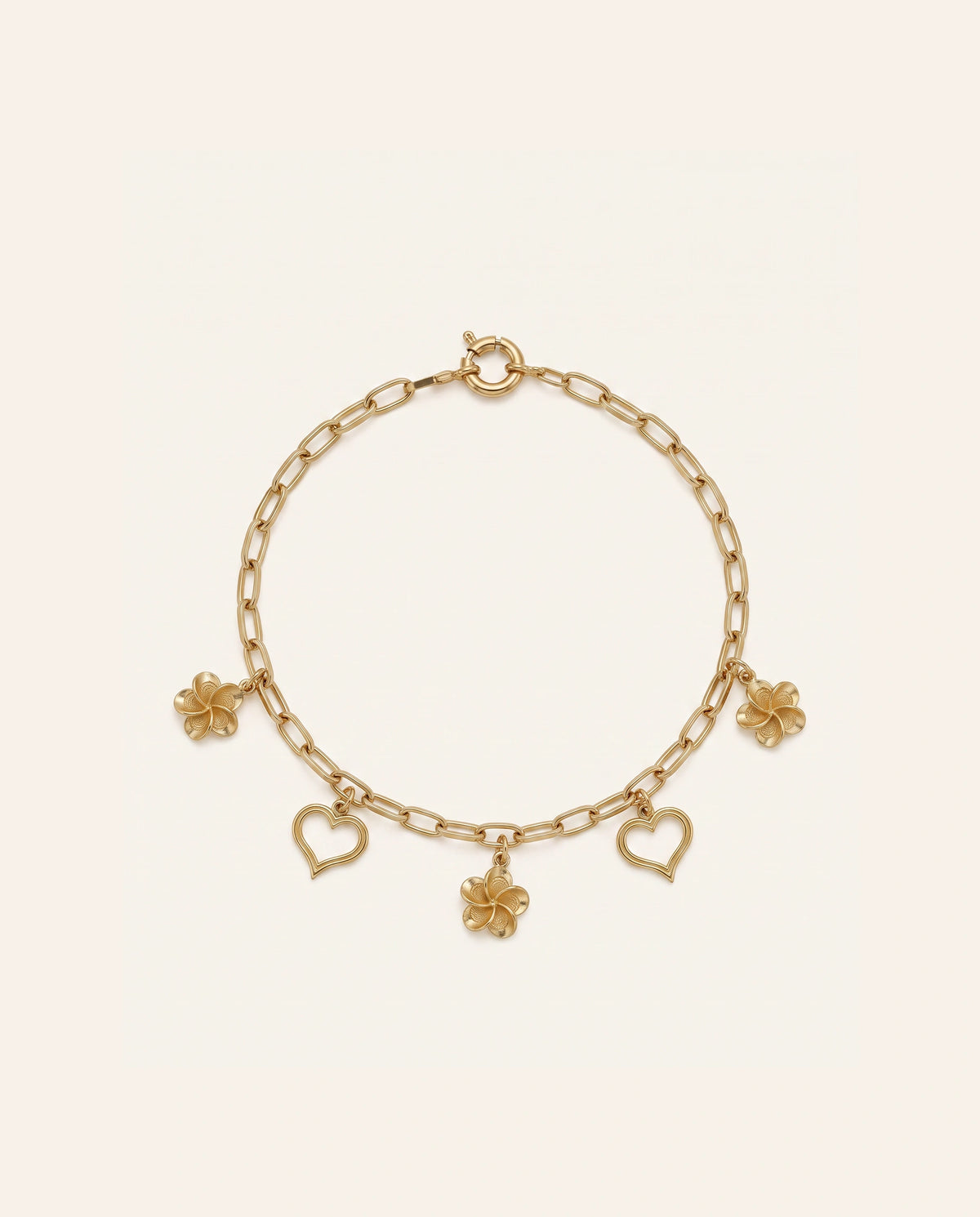 Yellow gold paperclip chain charm bracelet featuring dangling flowers and open hearts on an off-white background