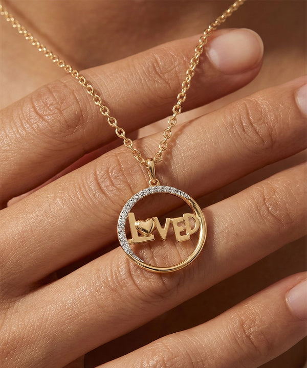 Gold necklace with 'LOVED' pendant on a hand