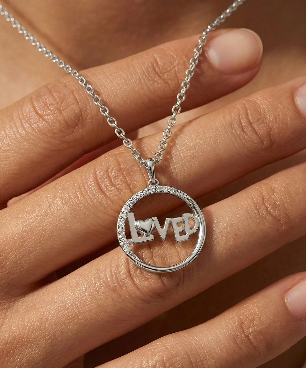 Silver necklace with 'LOVED' pendant on a hand