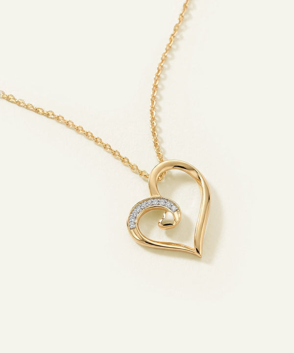 Gold heart-shaped necklace with a chain on a light beige background