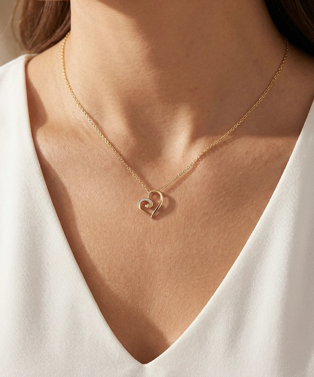 Gold heart-shaped necklace on a person wearing a white top