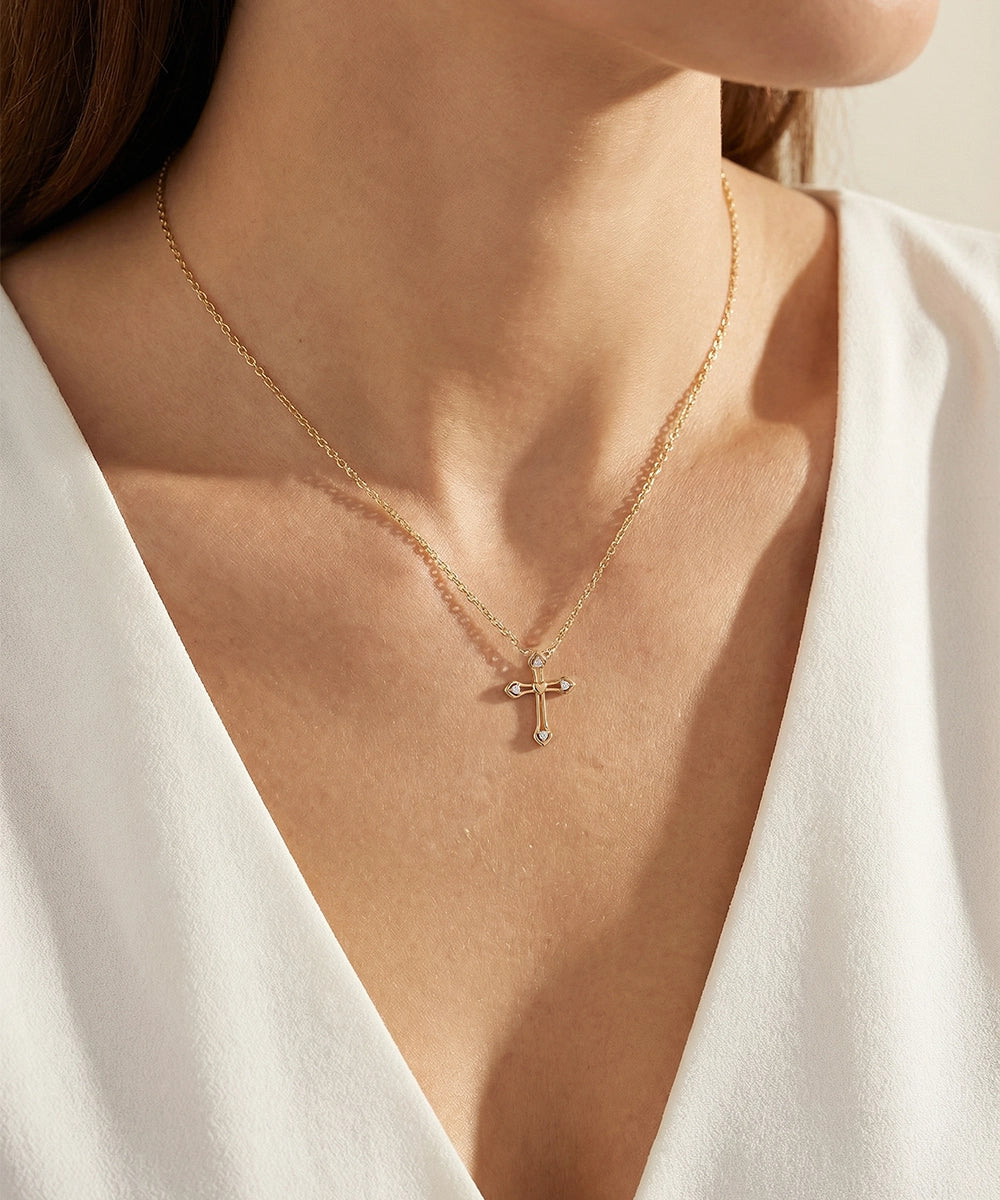 Gold necklace with a cross pendant worn by a person in a white outfit.