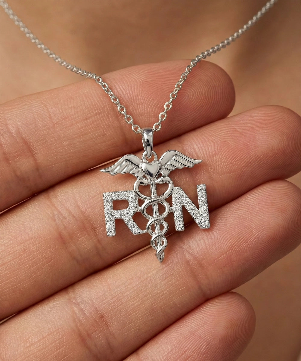 Silver 'RN' pendant with caduceus on a chain held in a hand against a blurred background