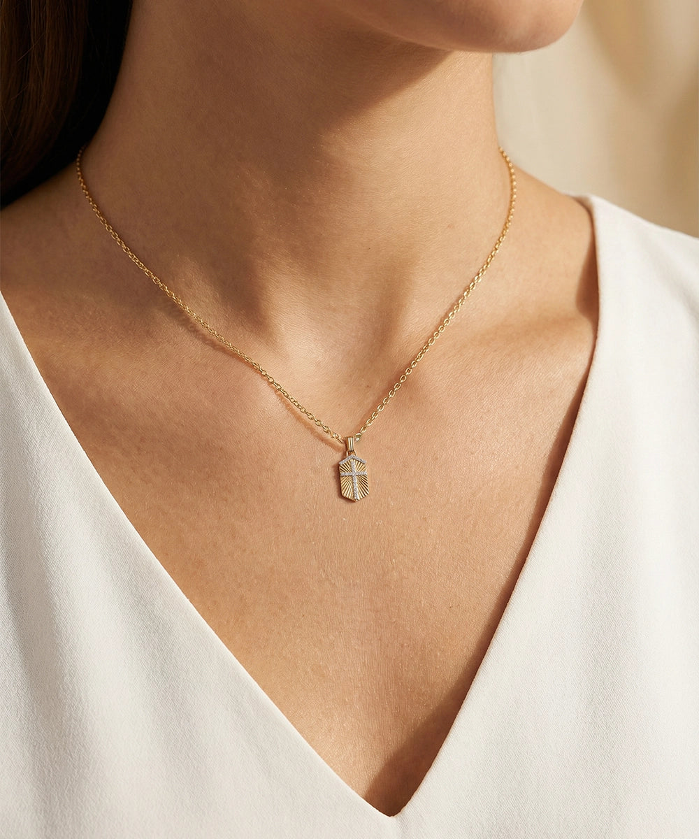 Gold necklace with a pendant on a person wearing a white top.