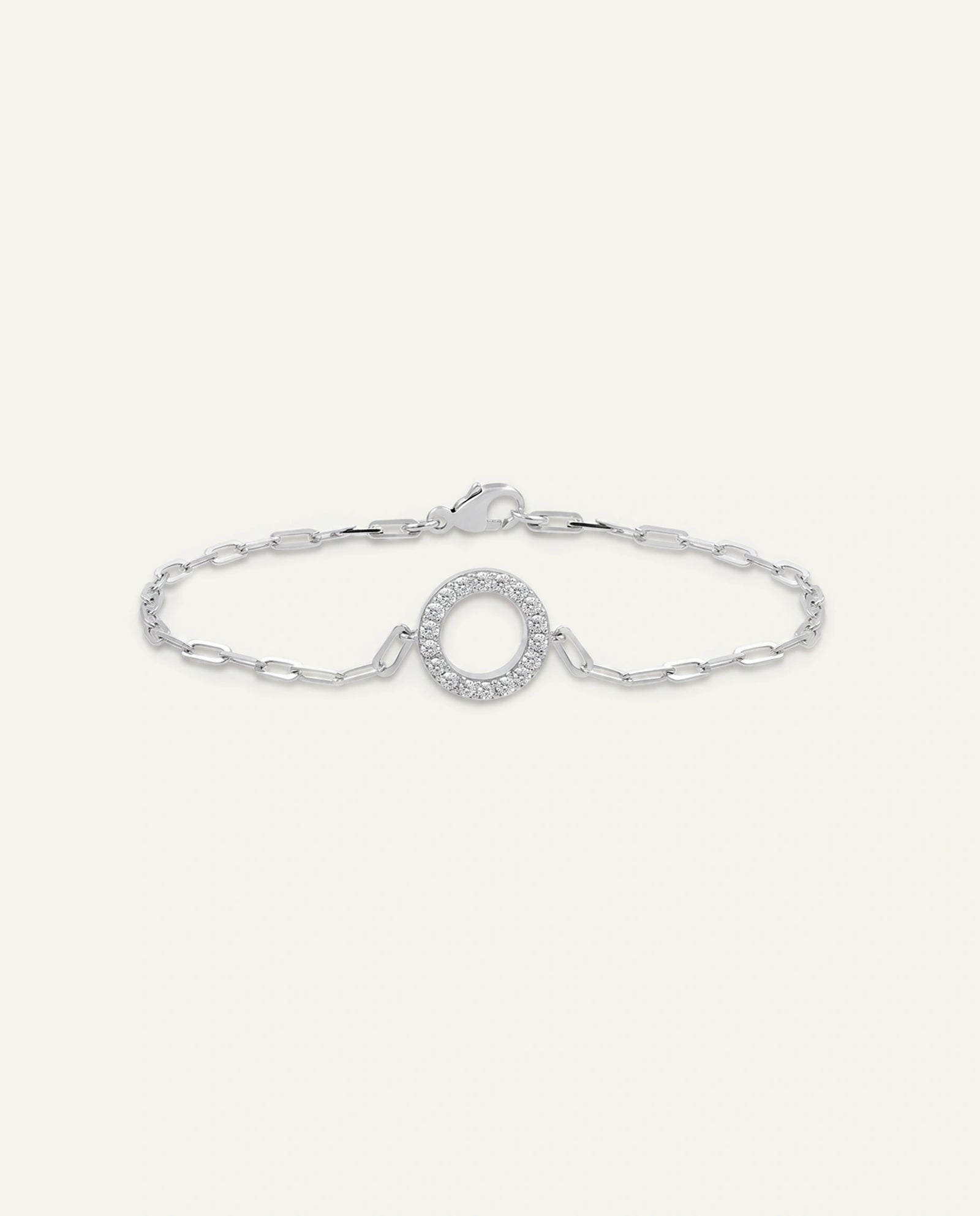 A silver chain bracelet featuring a central oval link set with small clear stones, photographed on a light cream background.