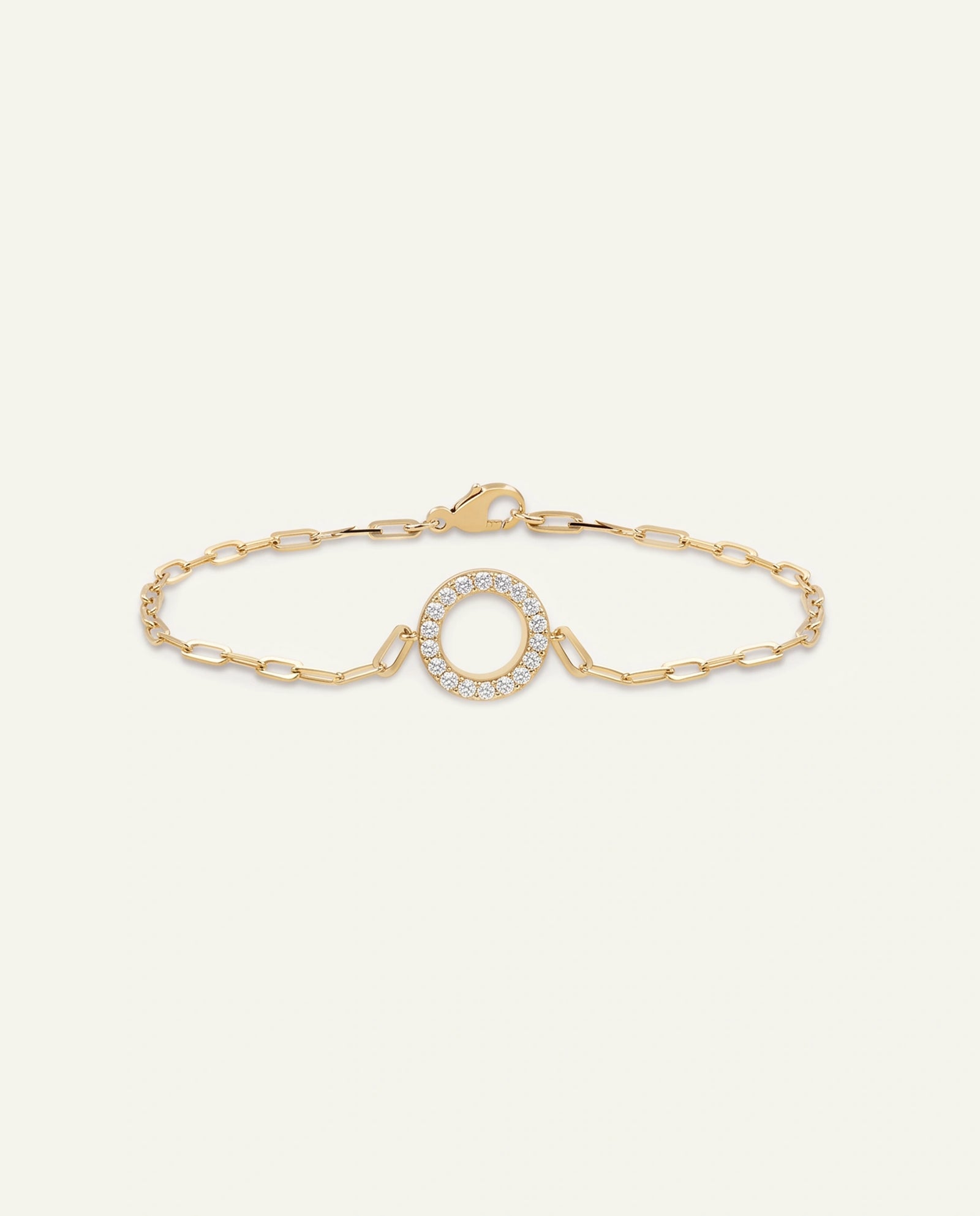 A delicate gold chain bracelet featuring a central oval motif bordered by small clear stones, displayed on a light cream background.