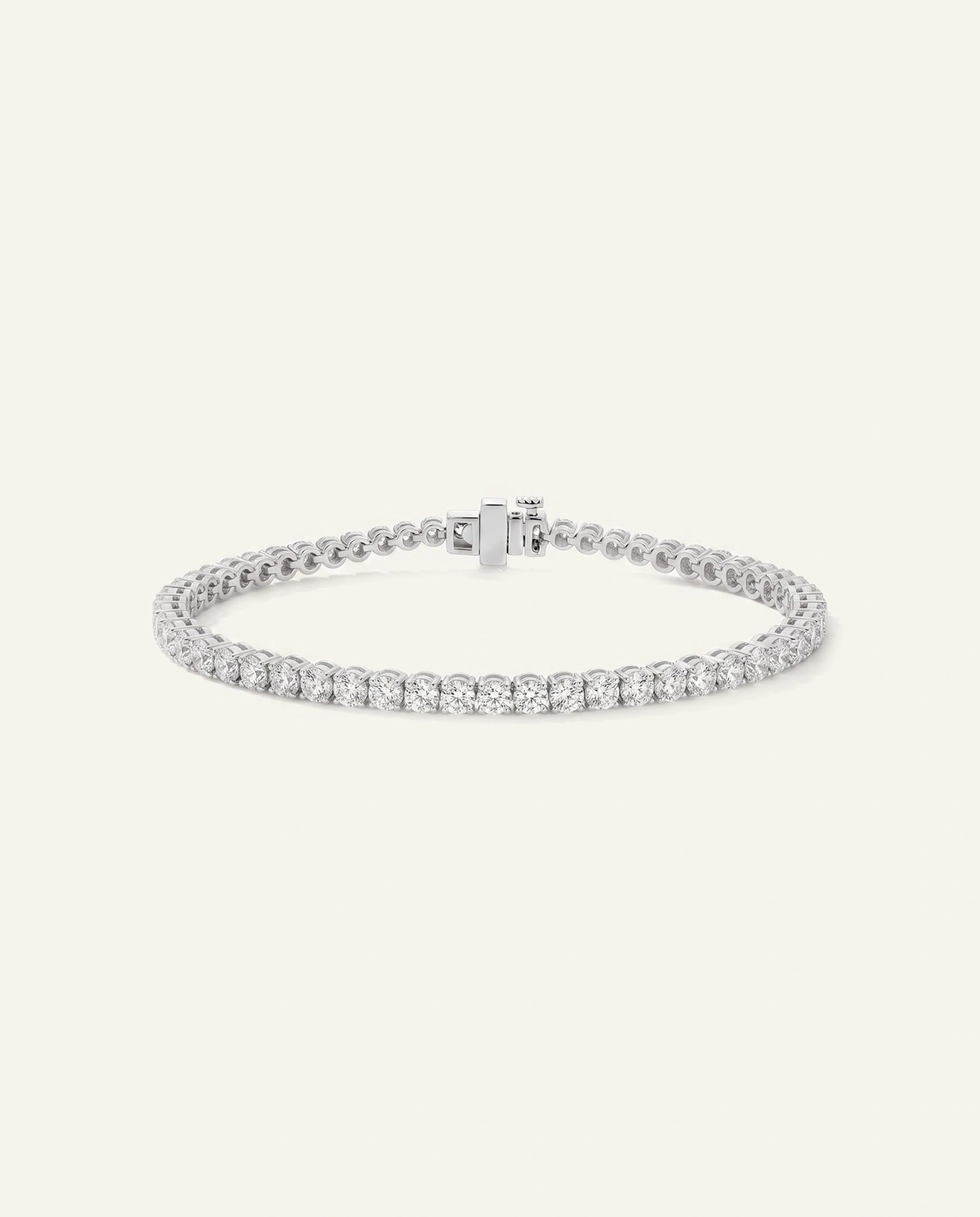 A silver tennis bracelet with a single row of round-cut clear stones, displayed on a light cream background.