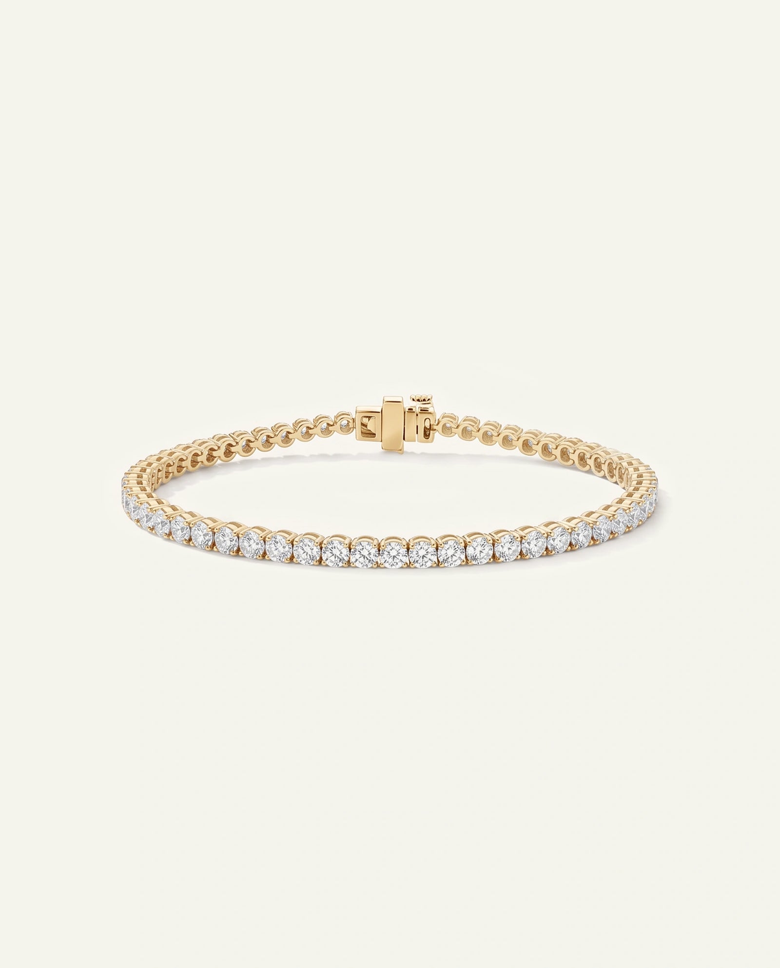 A gold tennis bracelet featuring a row of clear round-cut gemstones, displayed on a clean, light cream background.