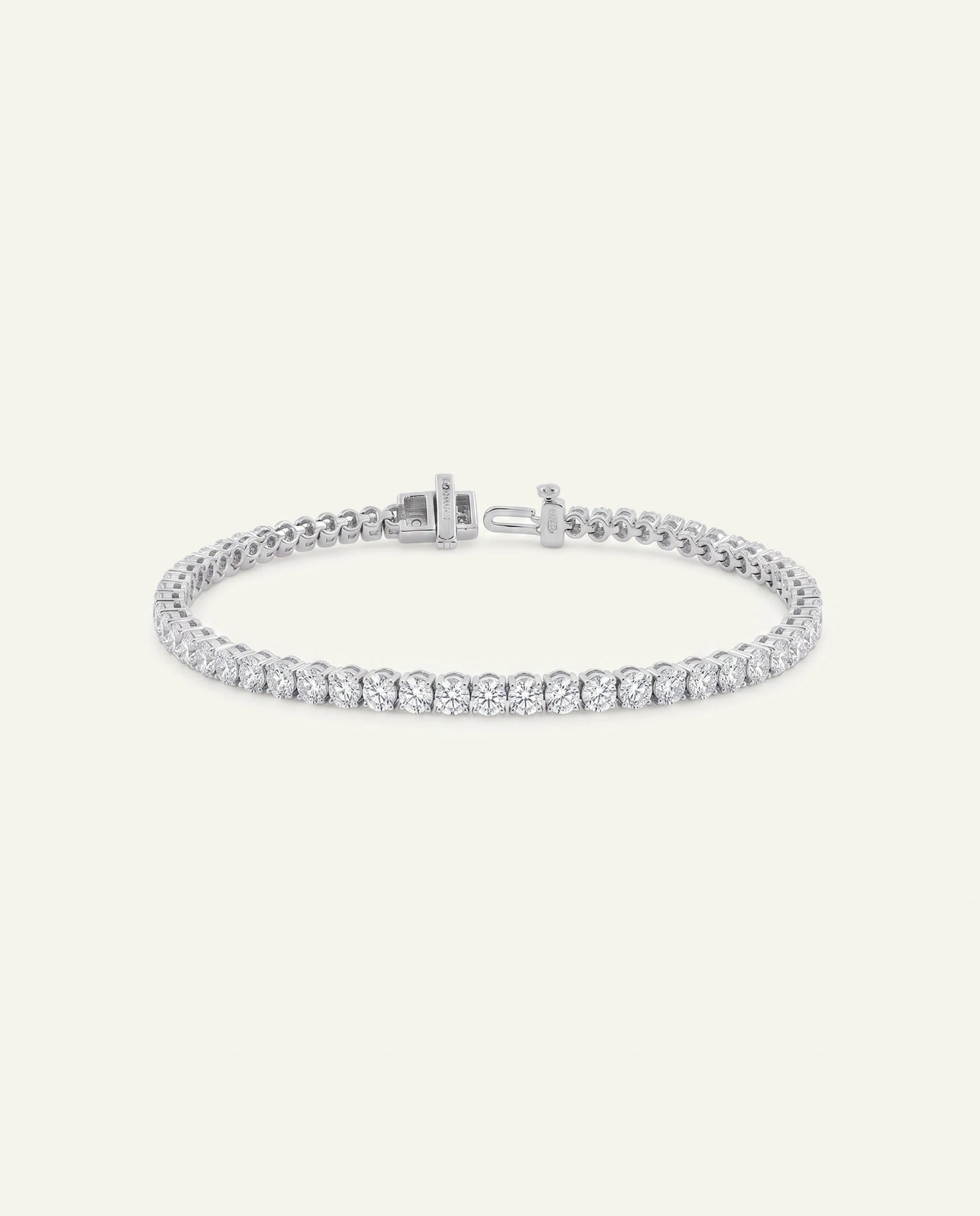 A silver tennis bracelet with a row of clear round-cut stones, displayed on a light cream background.