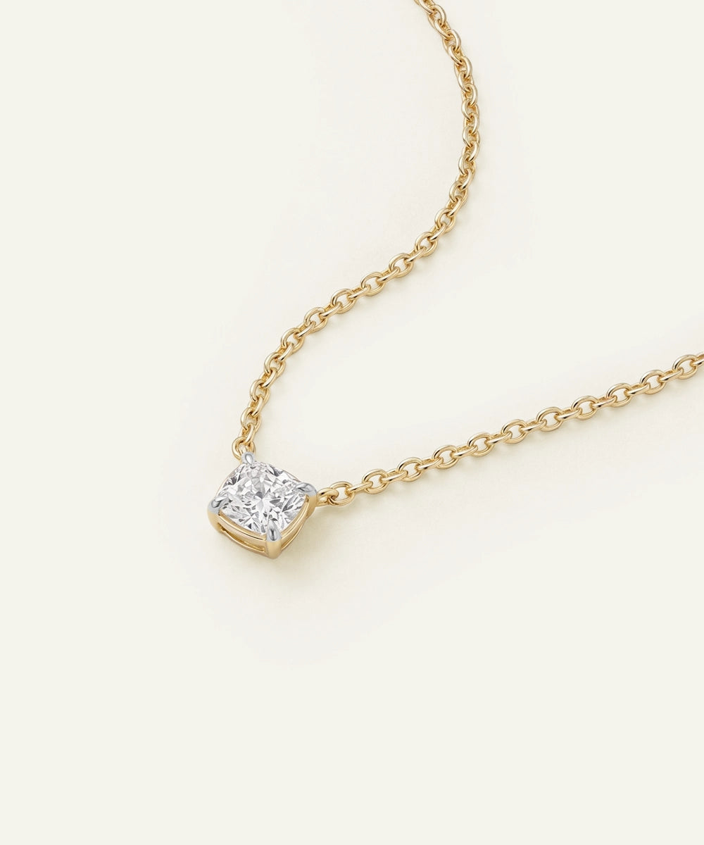 Gold necklace with a diamond pendant on a light beige background