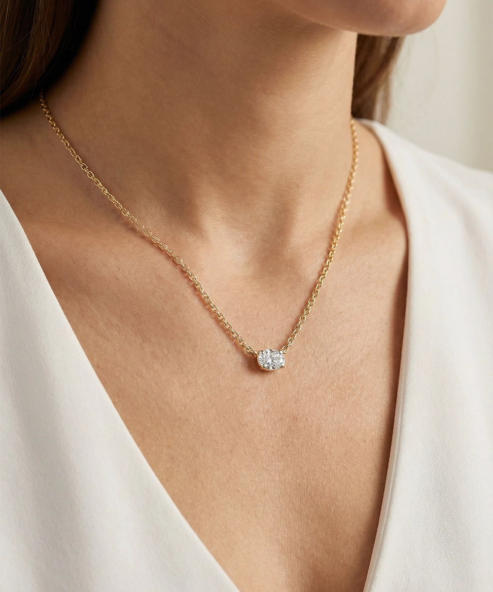Gold necklace with a diamond pendant worn by a person in a white outfit.