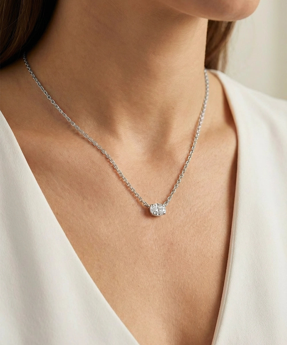 Silver necklace with a small diamond pendant worn by a person in a white outfit.