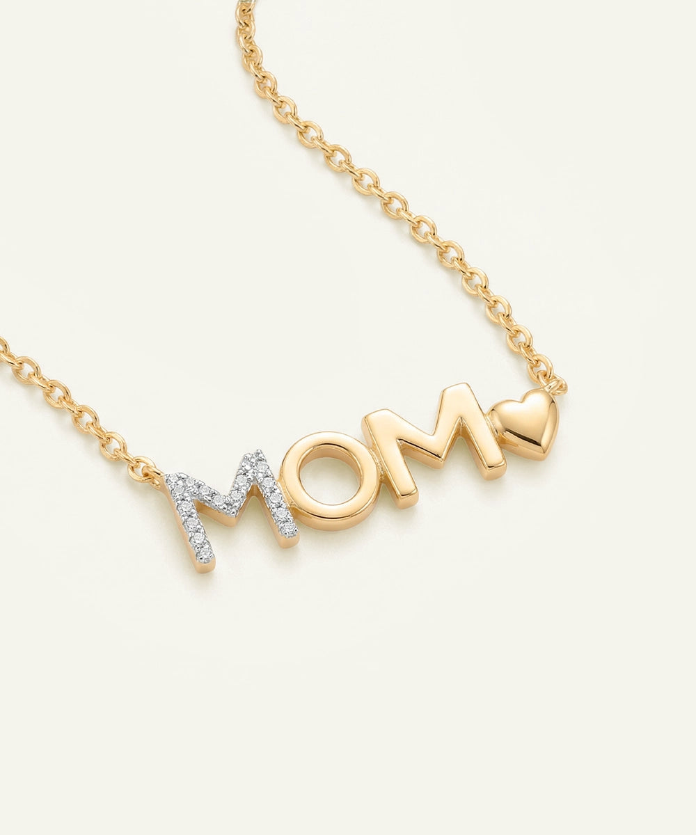 Gold necklace with 'MOM' pendant on a light beige background