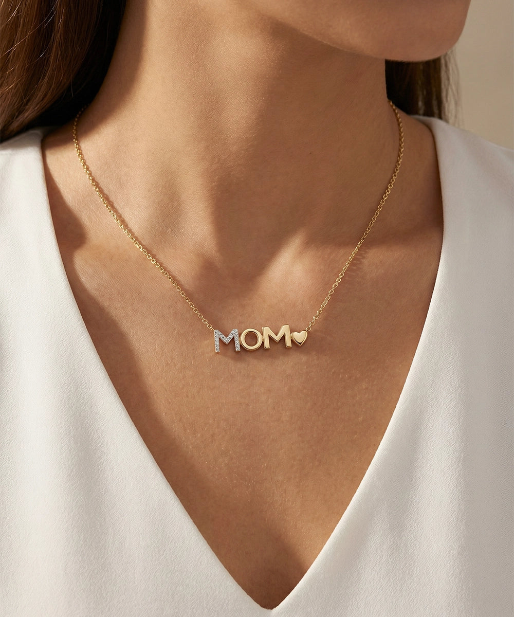 Gold necklace with 'MOM' pendant on a person wearing a white top.