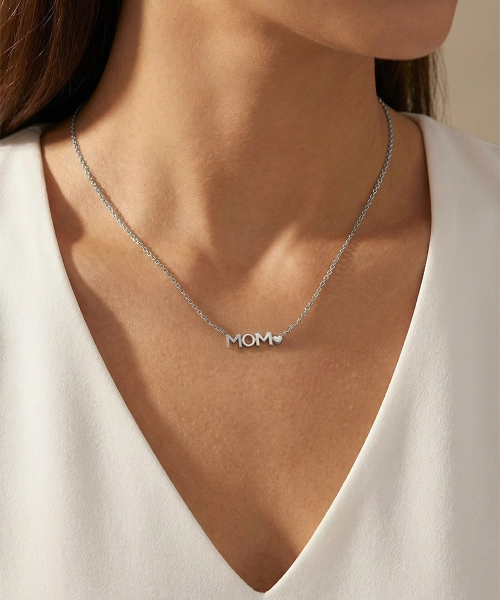 Silver 'MOM' necklace worn by a person in a white top.