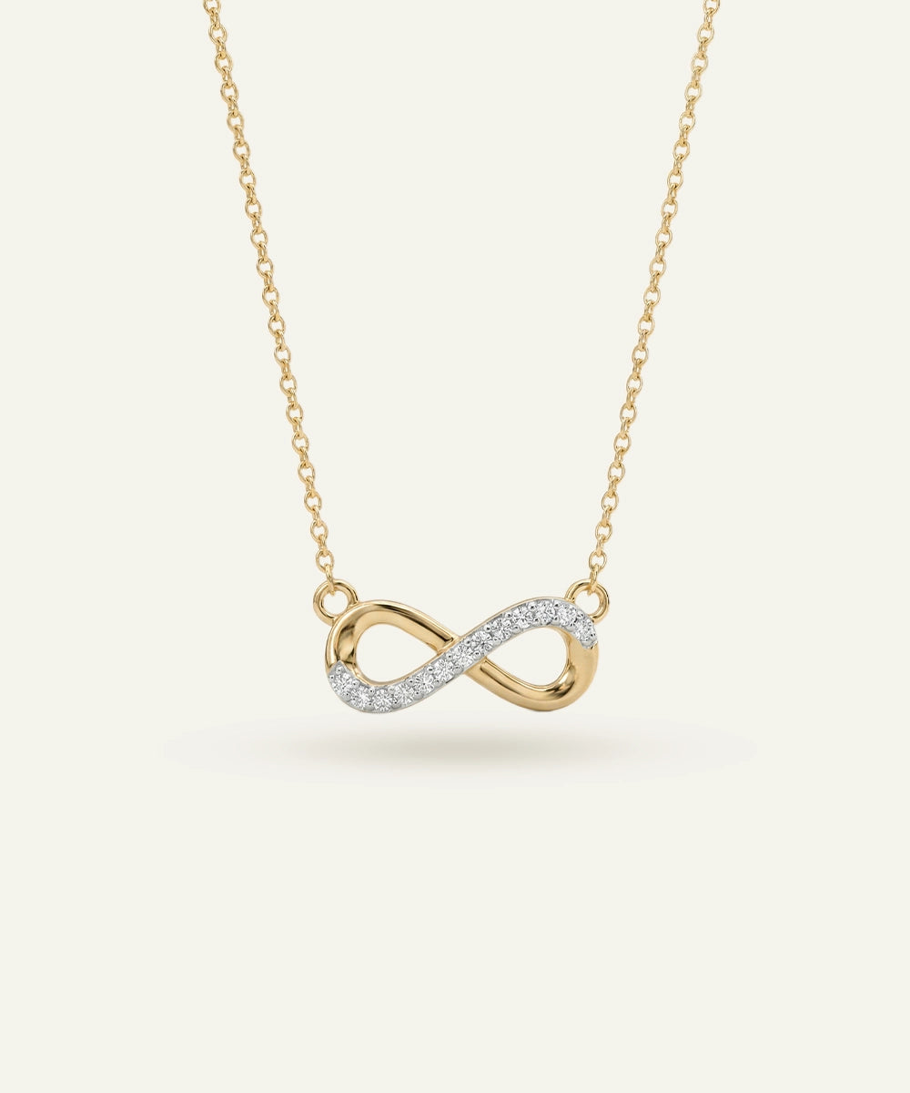 Gold infinity necklace with diamonds on a light beige background