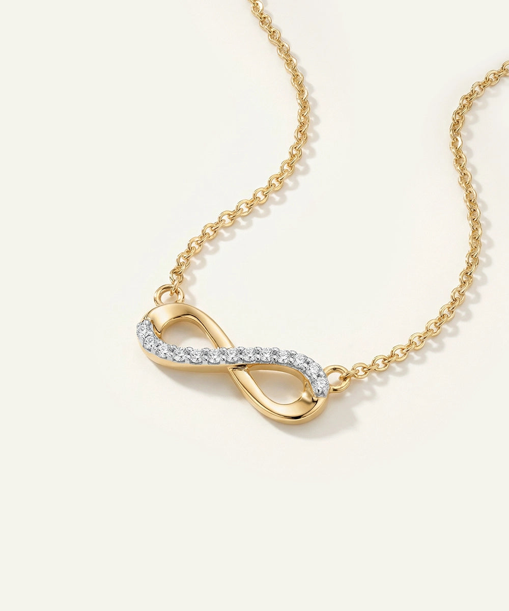 Gold infinity necklace with diamond accents on a light beige background