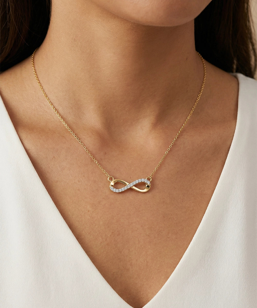 Gold infinity necklace with diamonds on a person wearing a white top
