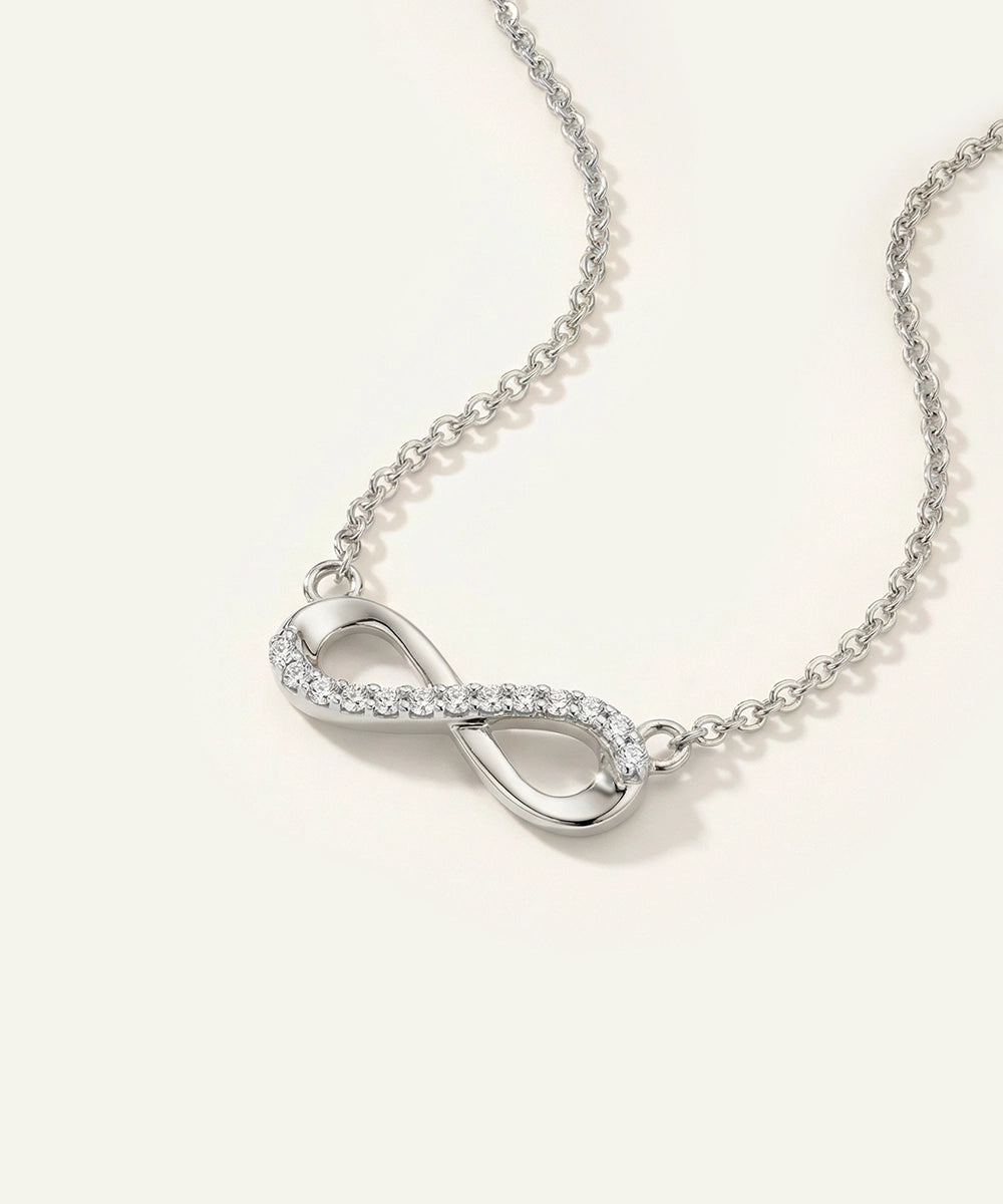 Silver infinity necklace with clear stones on a light beige background