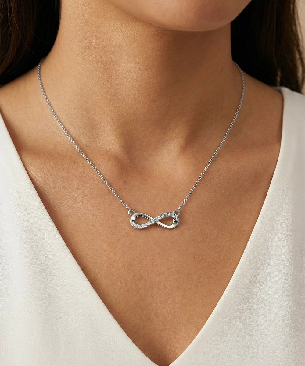 Silver infinity necklace on a person wearing a white top