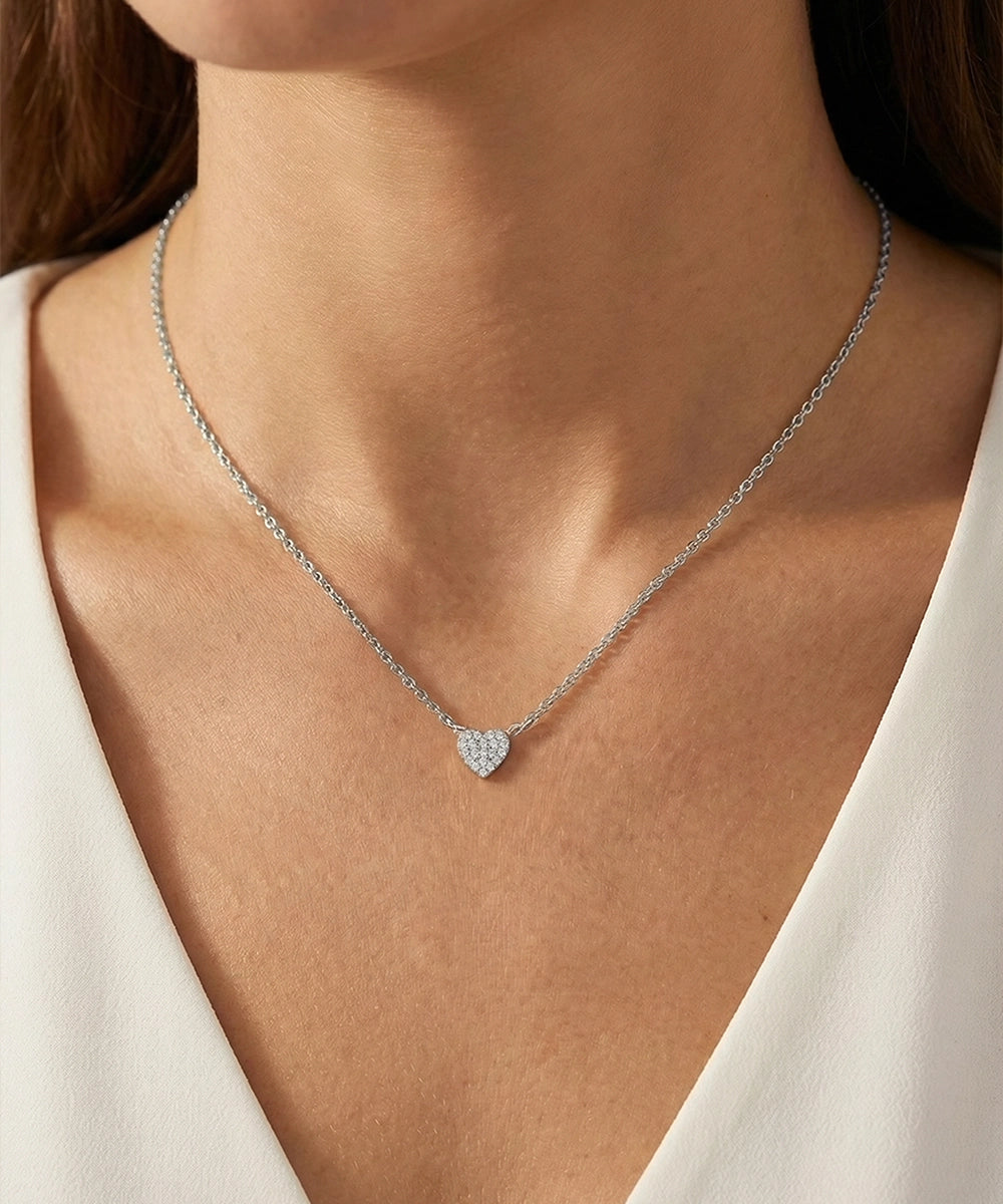 Necklace with a heart-shaped pendant worn by a person in a white outfit.