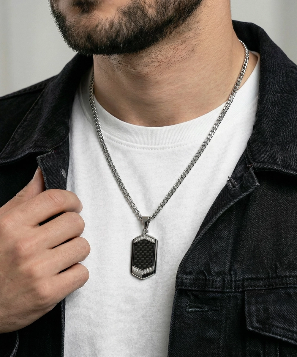 Man wearing a silver necklace with a black pendant on a plain background