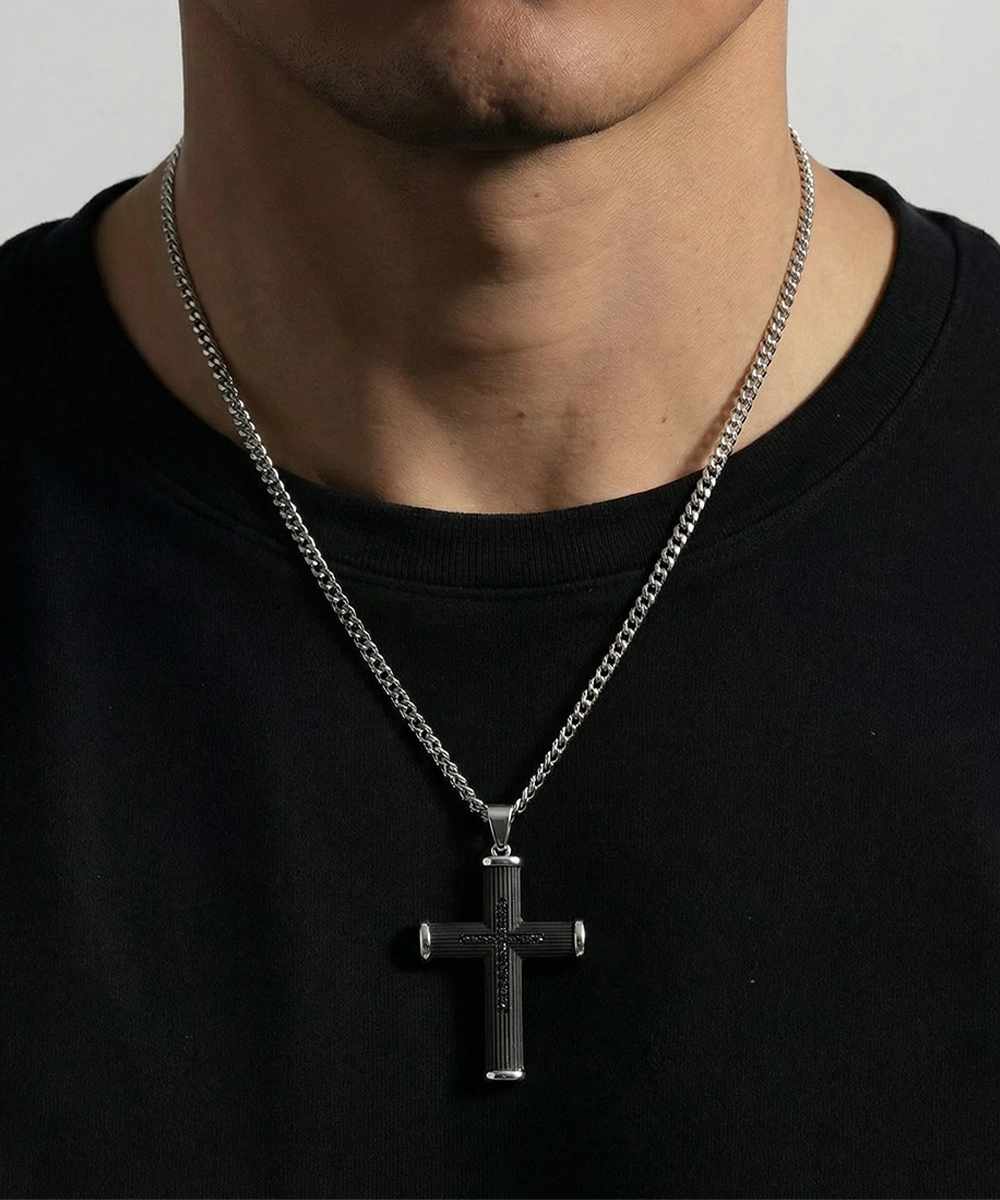 Person wearing a black cross pendant necklace on a plain background
