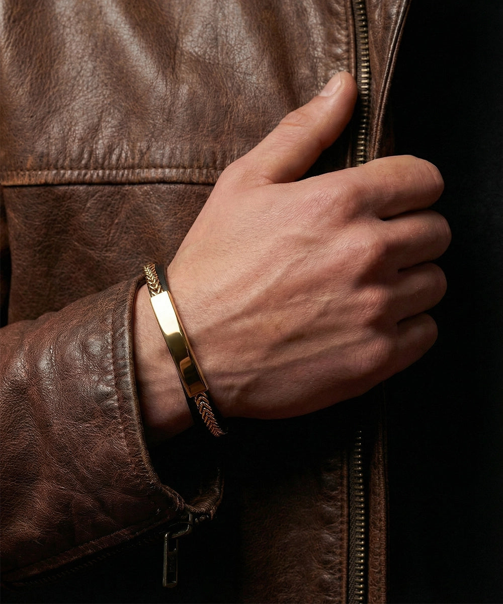 Hand wearing a gold bracelet on a brown leather jacket