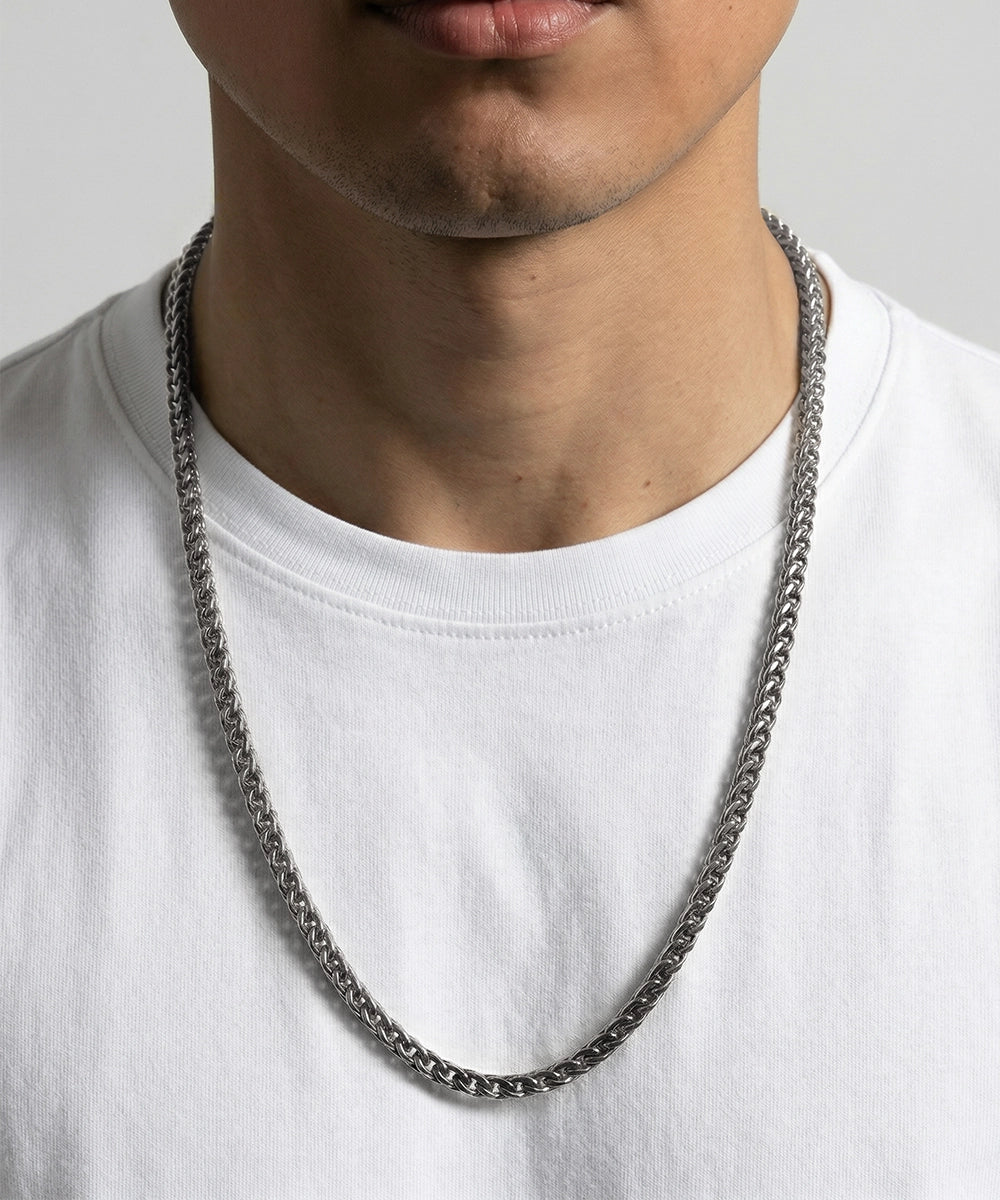 Person wearing a silver chain necklace on a plain background