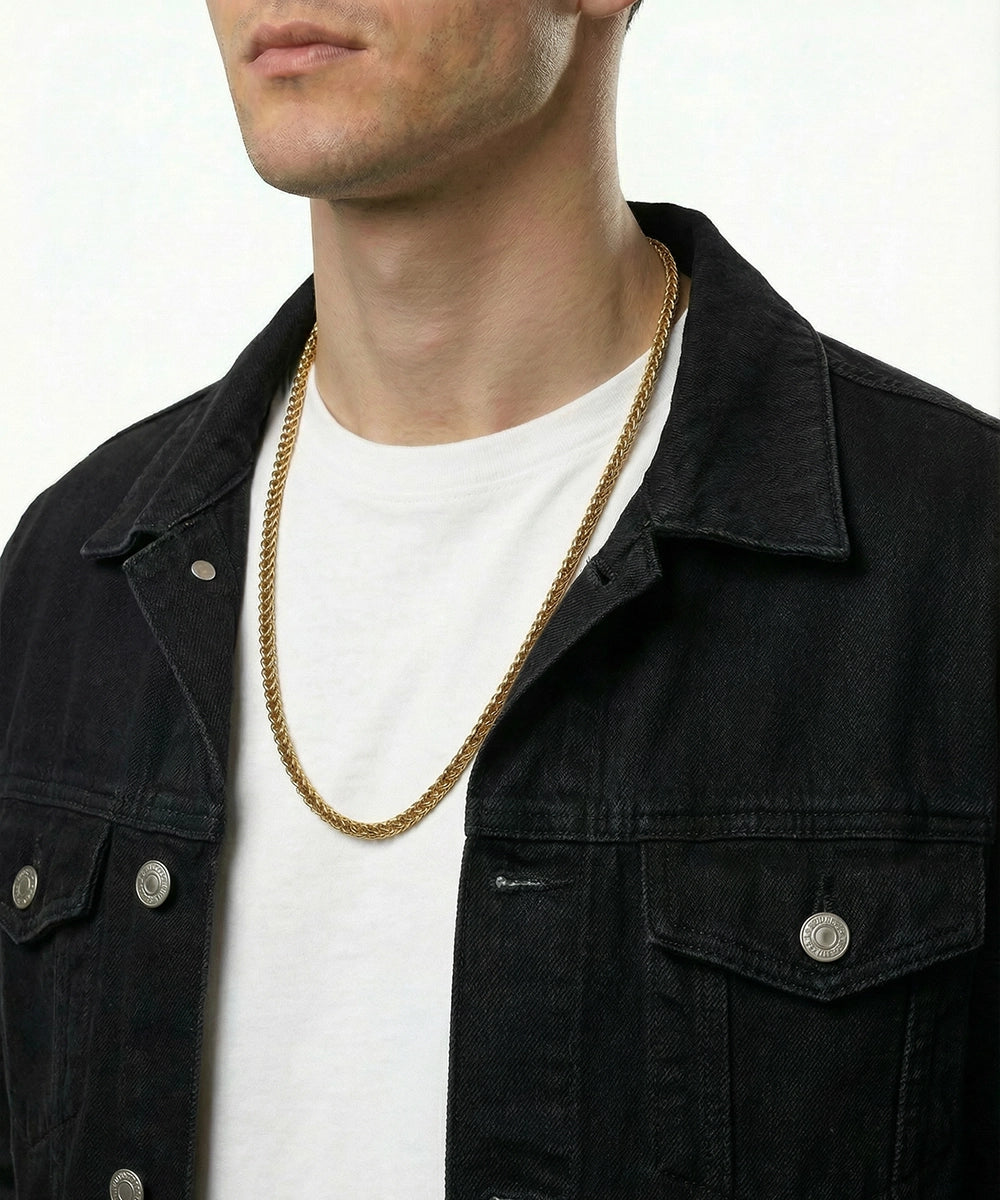 Man wearing a black jacket and white shirt with a gold chain necklace on a plain background