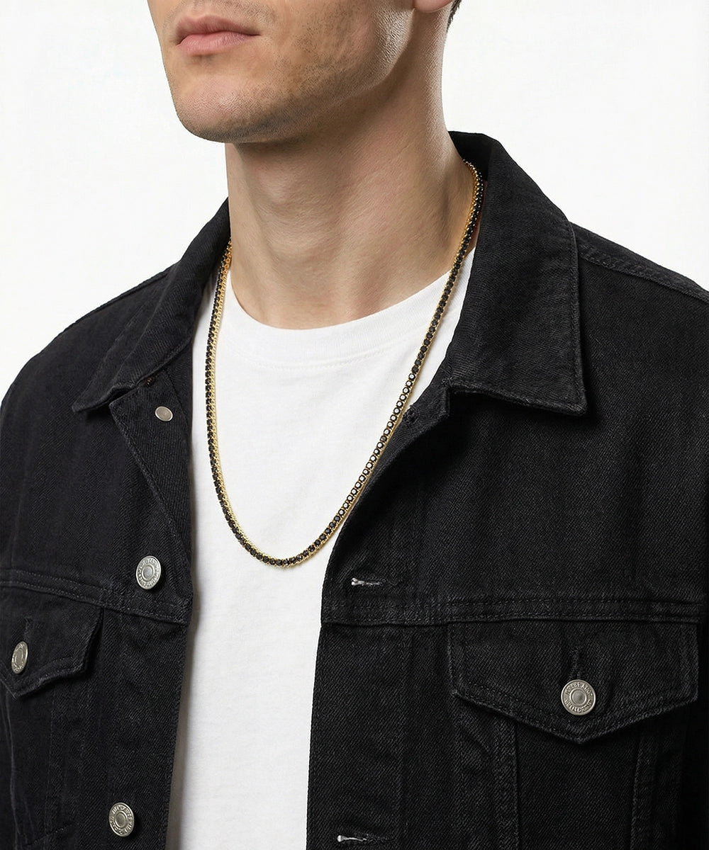 Man wearing a black jacket and white shirt with a gold chain necklace on a plain background