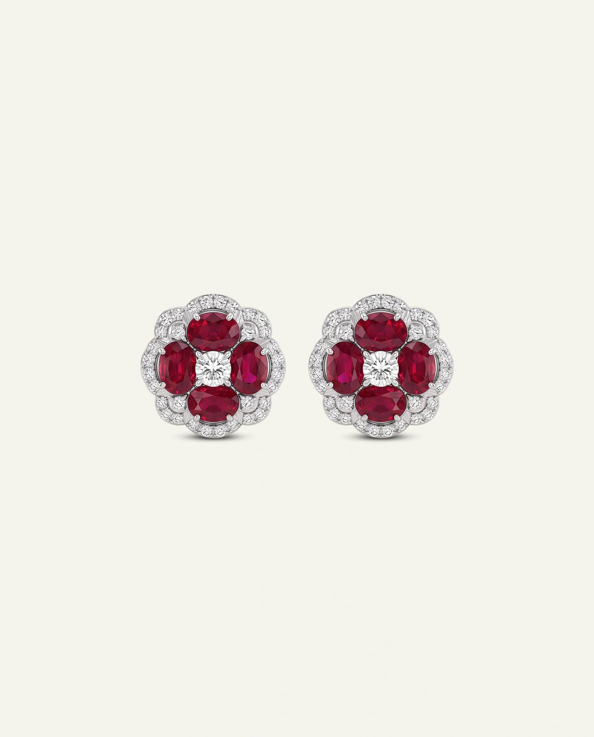 A pair of floral stud earrings featuring four round-cut deep red rubies surrounded by a halo of small clear stones, with a central round clear stone, set in a silver-toned metal on a light cream background.