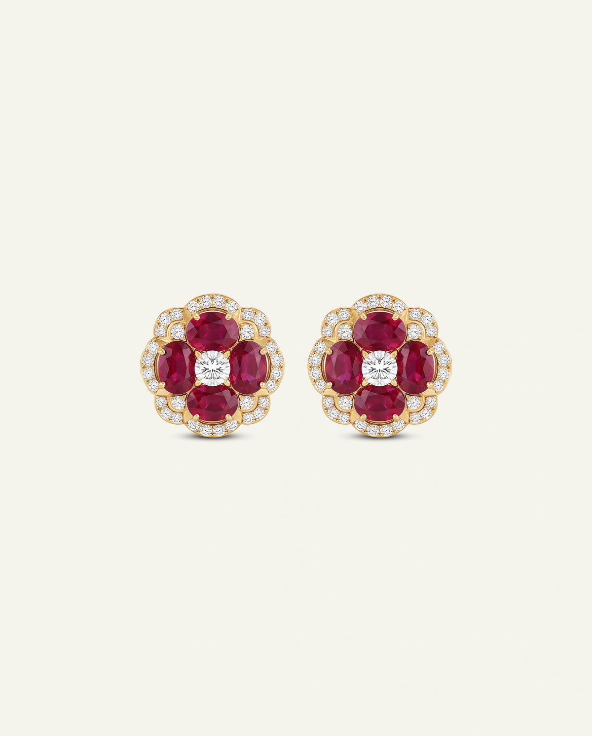 A pair of gold and ruby stud earrings with diamond accents, displayed on a light cream background.